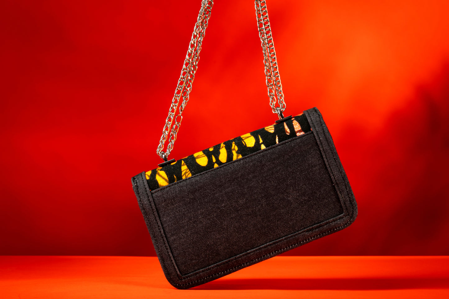 Back view of Ichaka African print and denim bag with bold orange and black Ankara pattern, accented by a silver chain strap.