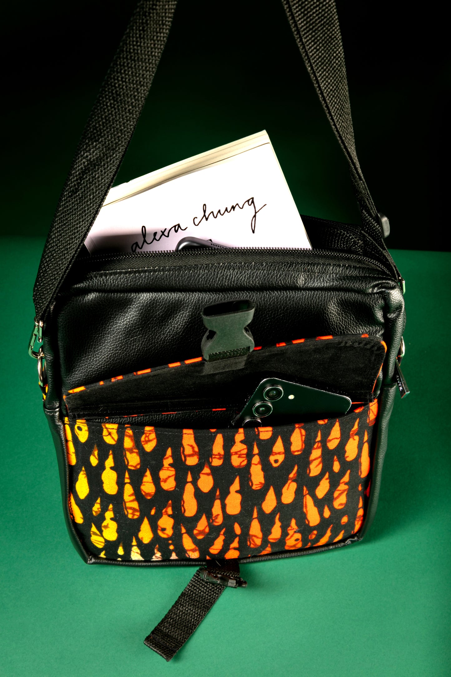 Top view of the Krar African Print Crossbody Bag featuring black faux leather and vibrant orange Ankara fabric, with a front flap pocket and buckle strap