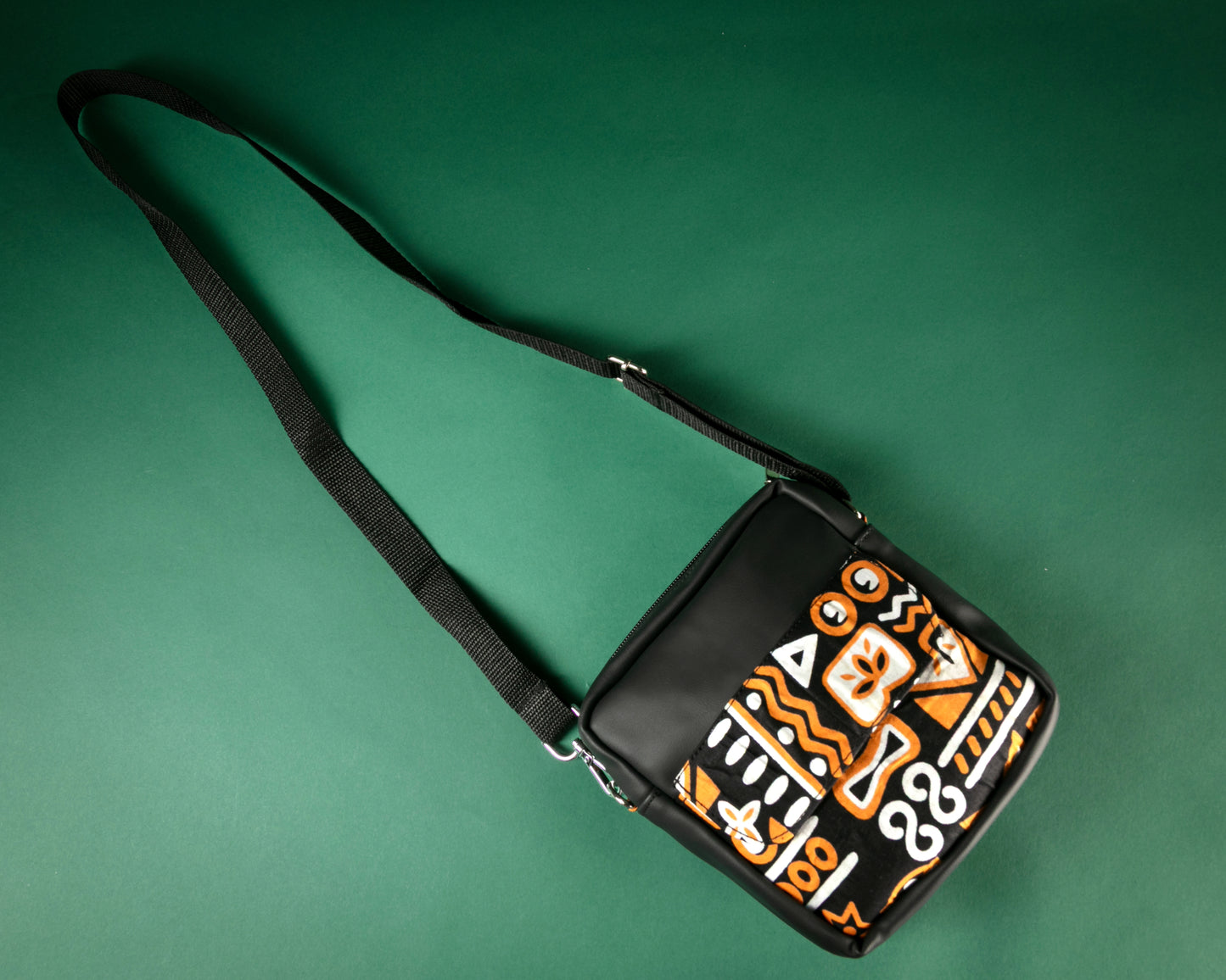 Flat Lay of black crossbody bag with brown, black & white tribal patterns on a green background