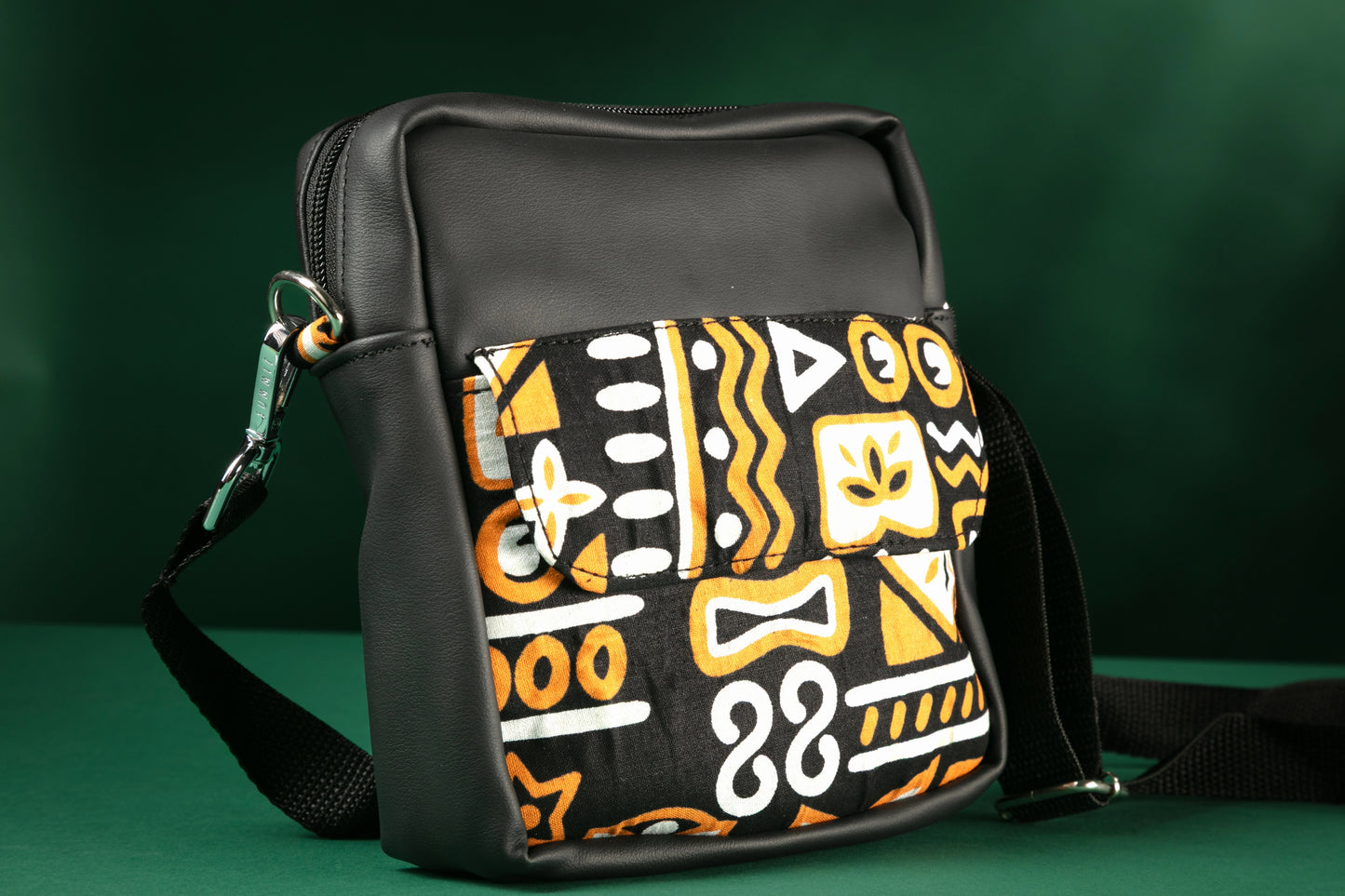 Black crossbody bag with brown, black & white tribal patterns on a green background