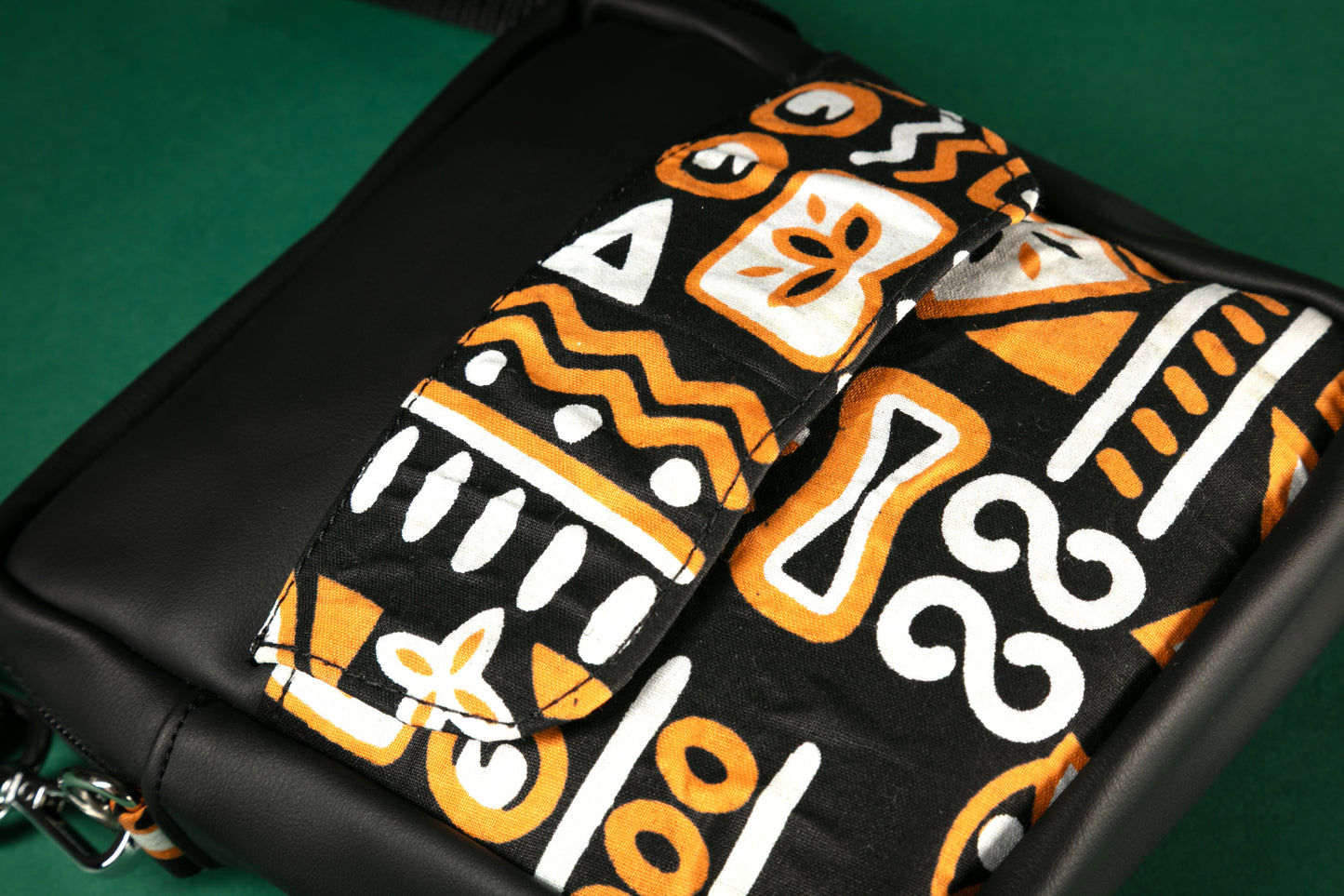 Flat Lay of black crossbody bag with brown, black & white tribal patterns on a green background