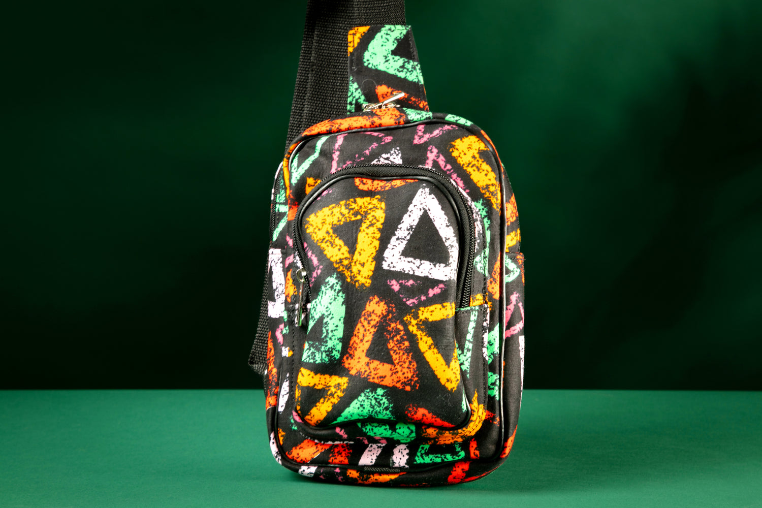 Adungu African Print Chest Fanny with bold multicolored triangular patterns, black adjustable strap, and front zipper pocket, displayed against a green background.