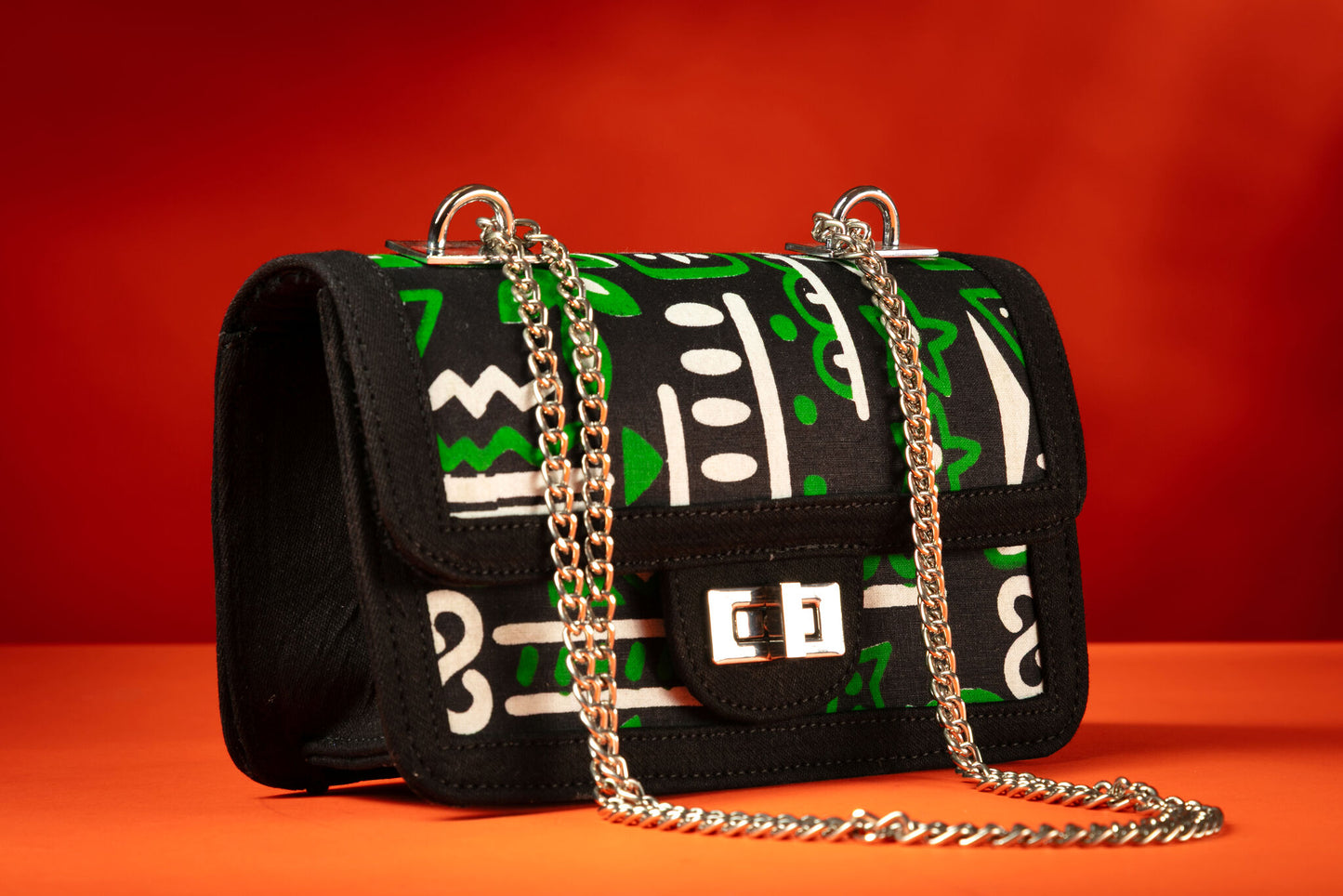 Side angle of Axatse African print and denim bag with bold green, white, and black Ankara pattern, accented by a silver chain strap