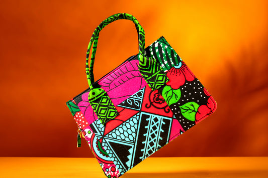 Front view of the Balangi Bag – a structured African print handbag featuring a multicolor design with contrasting green patterned handles, photographed against a warm orange background.