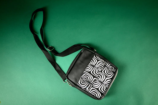 Flat Lay of Black crossbody bag with a black and white tribal pattern on a green background