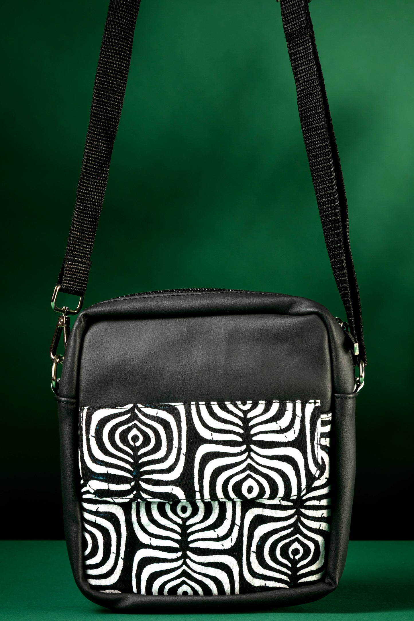 Front view of black crossbody bag with a black and white tribal pattern on a green background