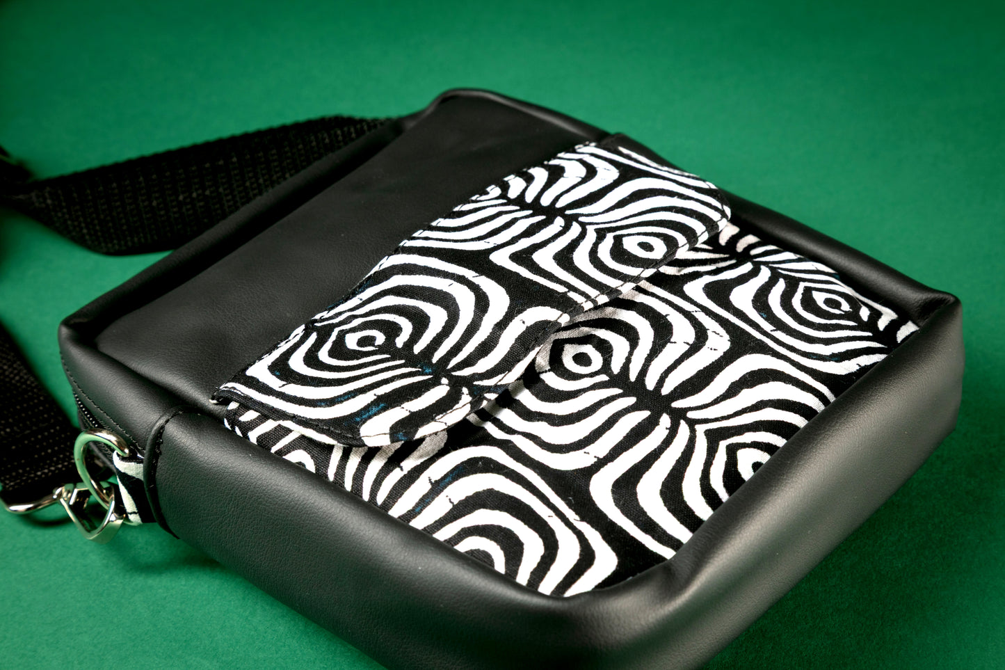 Flat Lay of black crossbody bag with a black and white tribal pattern on a green background