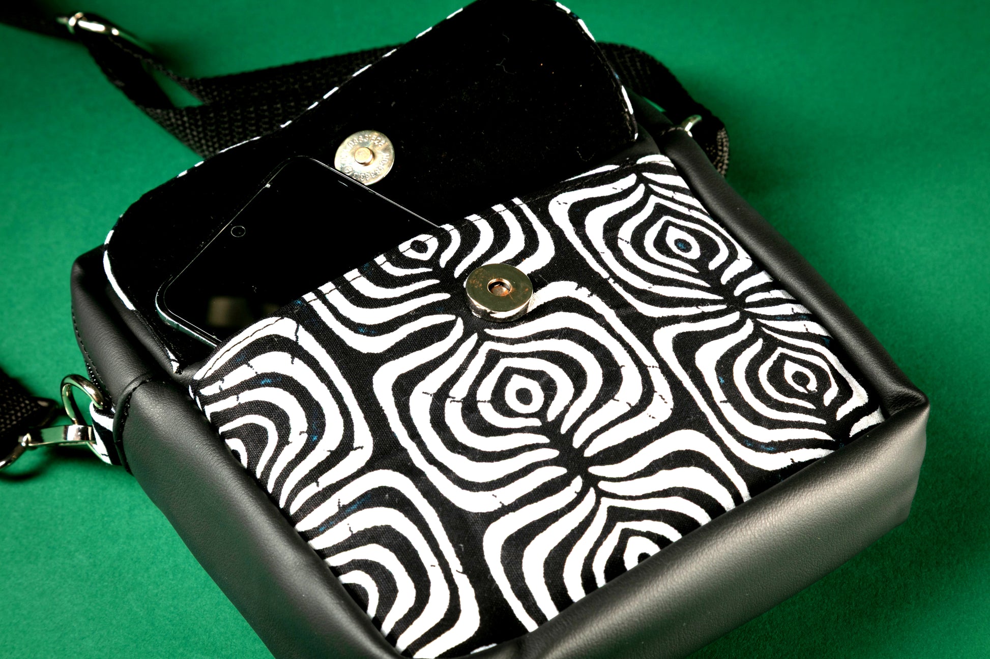 Black crossbody bag with a black and white tribal pattern with front pocket flap opened on a green background