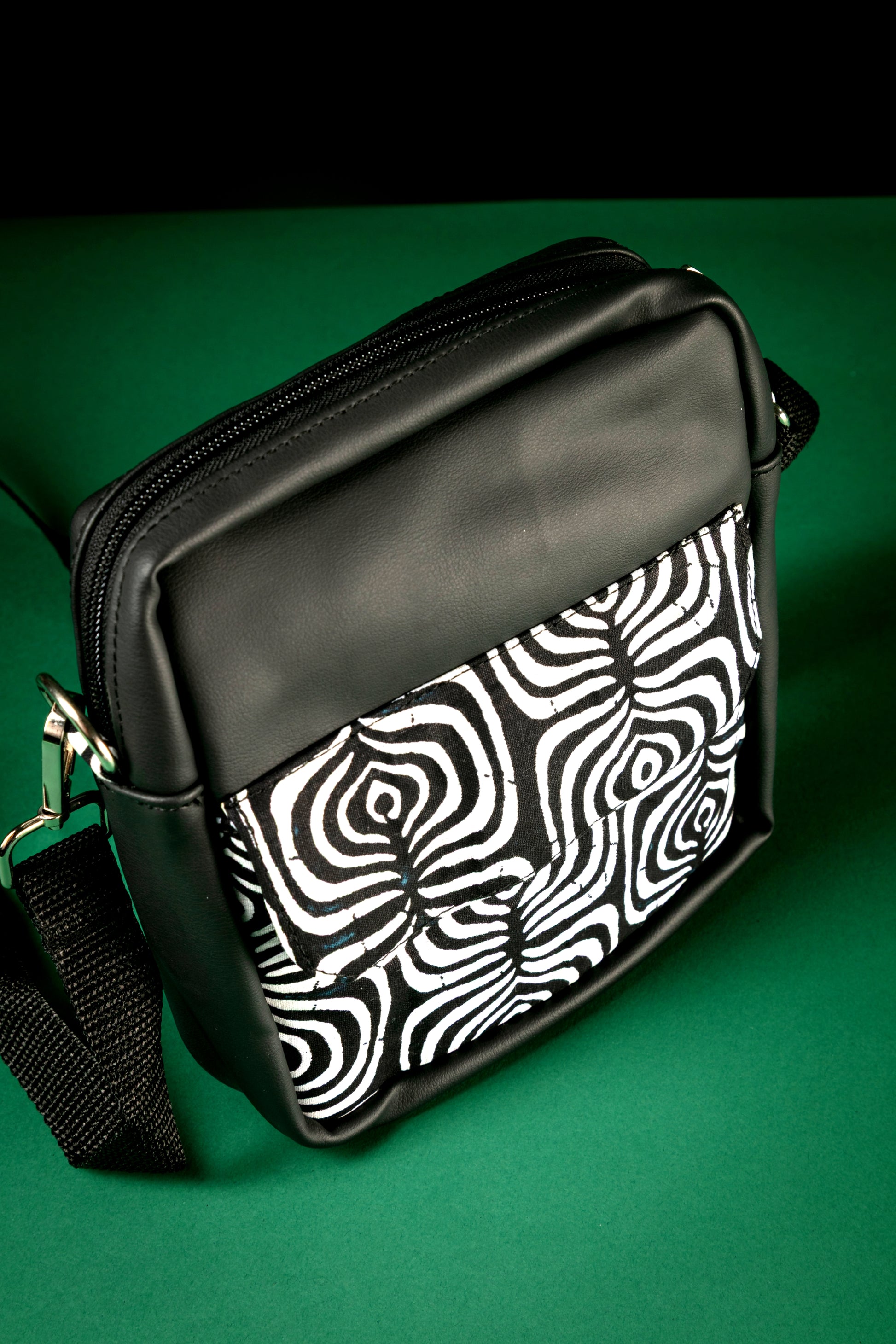 Angled view of black crossbody bag with a black and white tribal pattern on a green background