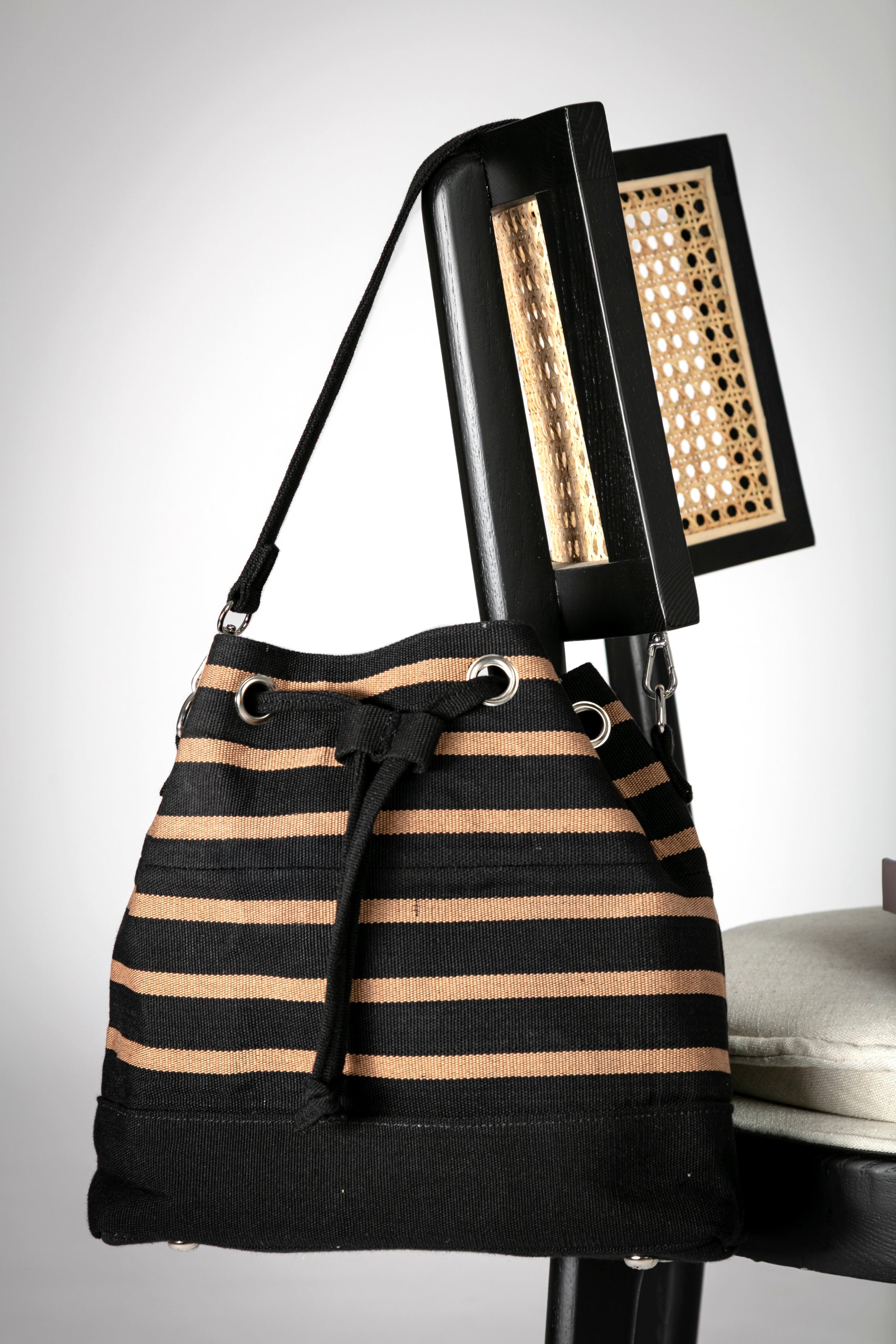 Black and beige striped bucket bag with short strap and a drawstring closure hanging on a chair