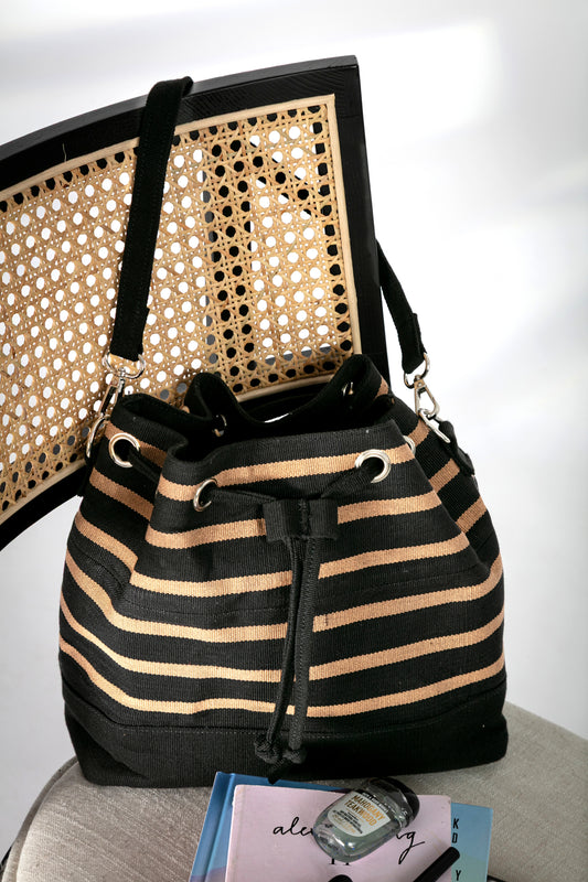 Black and beige striped bucket bag with short strap and a drawstring closure on a chair
