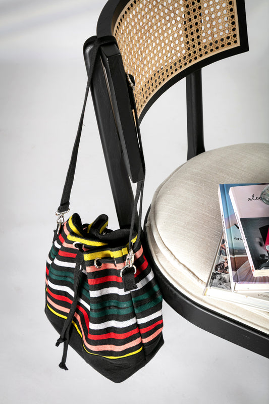 Multicolor striped bucket bag with long strap and a drawstring closure hanging on a chair