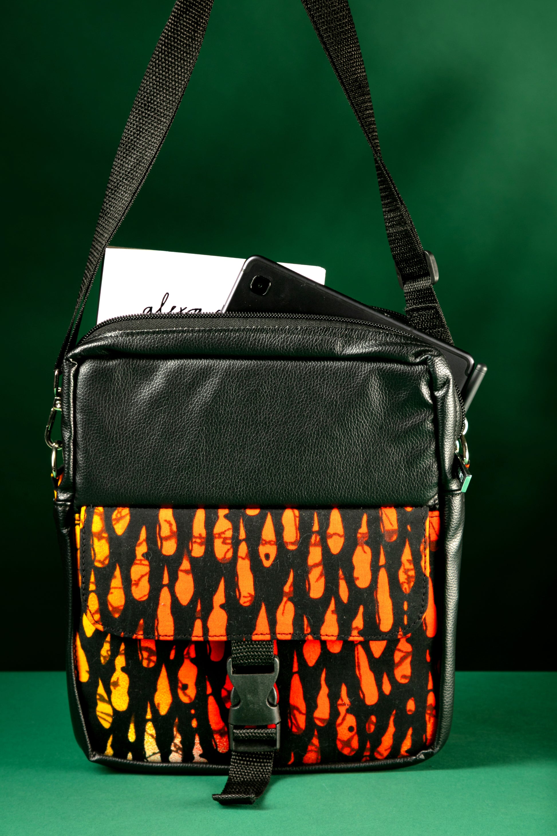 Krar African Print Crossbody Bag featuring black faux leather and vibrant orange Ankara fabric, with a front flap pocket, buckle strap, and adjustable shoulder strap.

