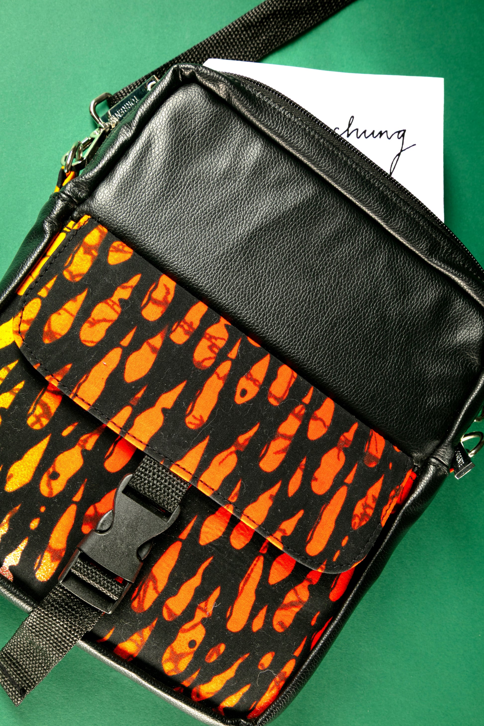 Close-up of the Krar African Print Crossbody Bag featuring black faux leather and vibrant orange Ankara fabric, with a front flap pocket and buckle strap