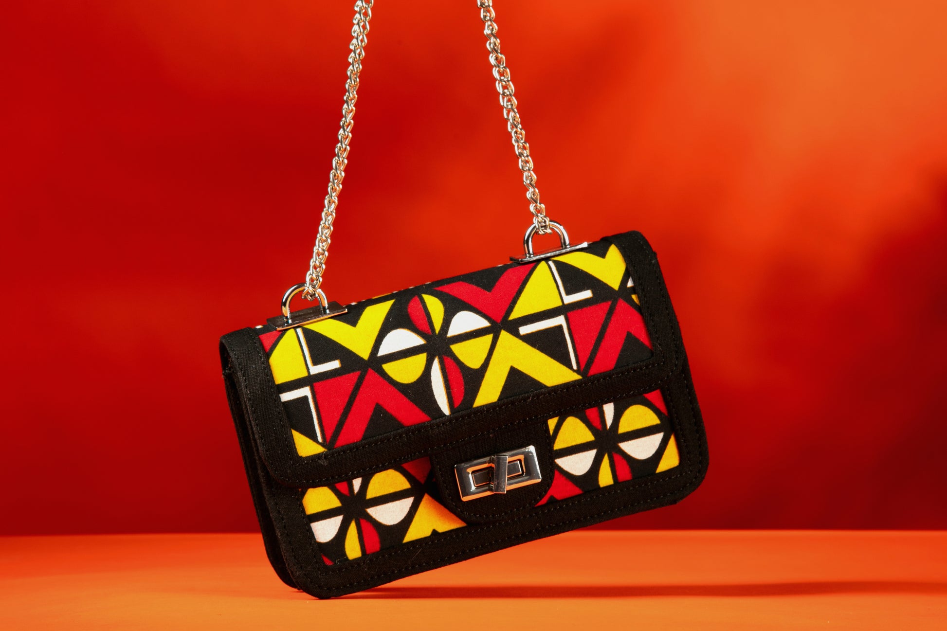 Closeup of the Shekere African print handbag with yellow, red, black and white Ankara fabric and black denim trim, featuring a silver chain strap and chrome twist-lock closure, handmade in Nigeria.