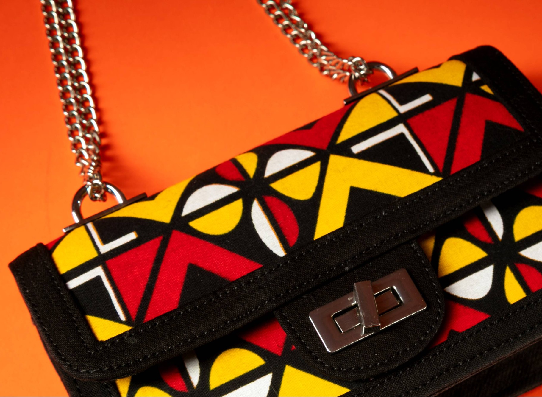 closeup of Shekere African print and denim bag with bold yellow, red, white, and black Ankara pattern, accented by a silver chain strap.