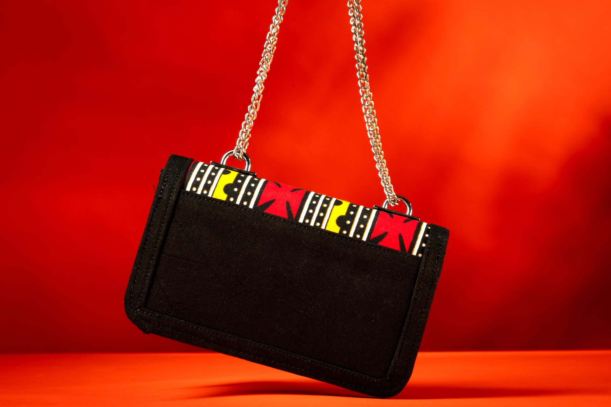 back view of Shekere African print and denim bag with bold yellow, red, white, and black Ankara pattern, accented by a silver chain strap.