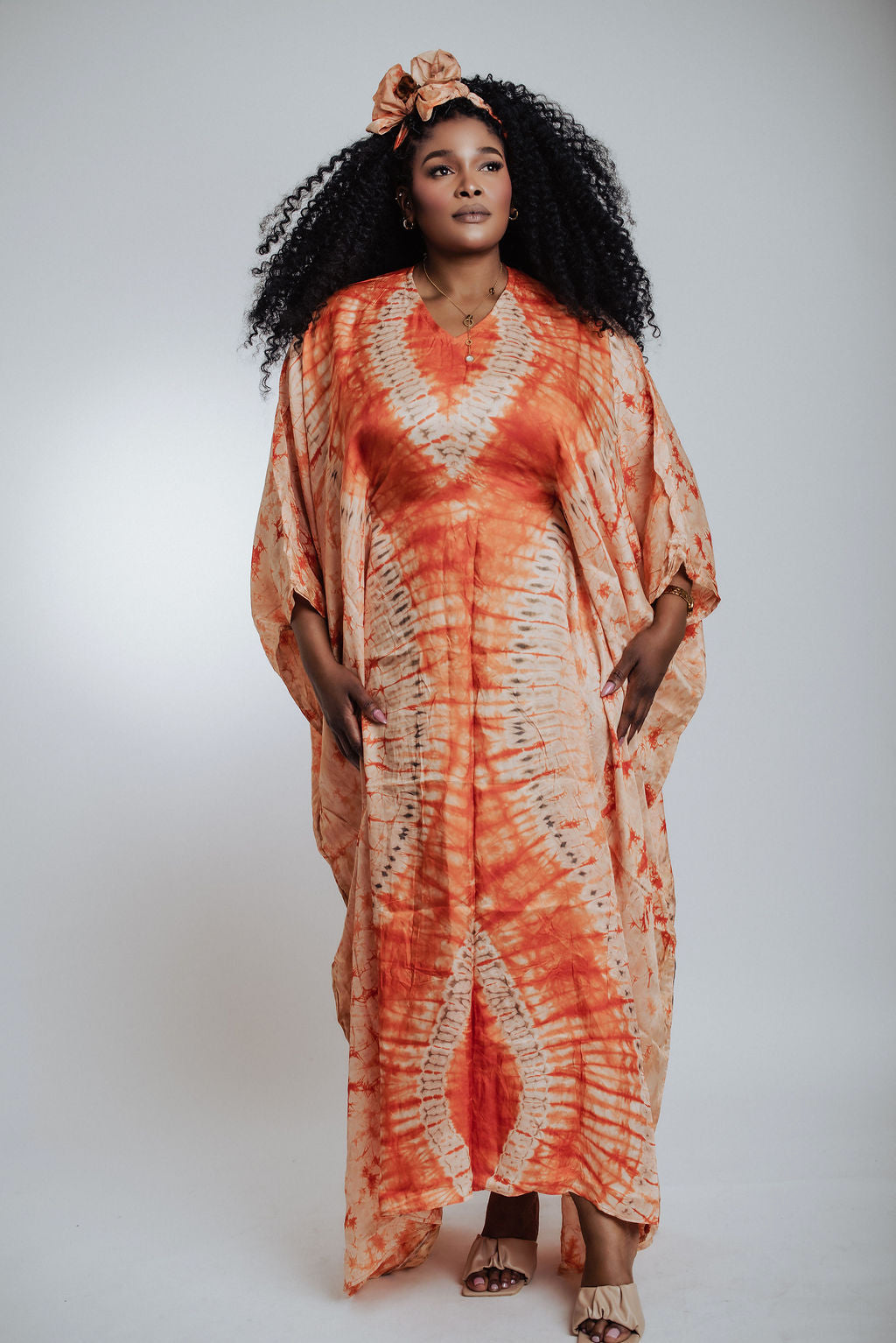 Woman wearing an orange tie-dye dress with a plain background