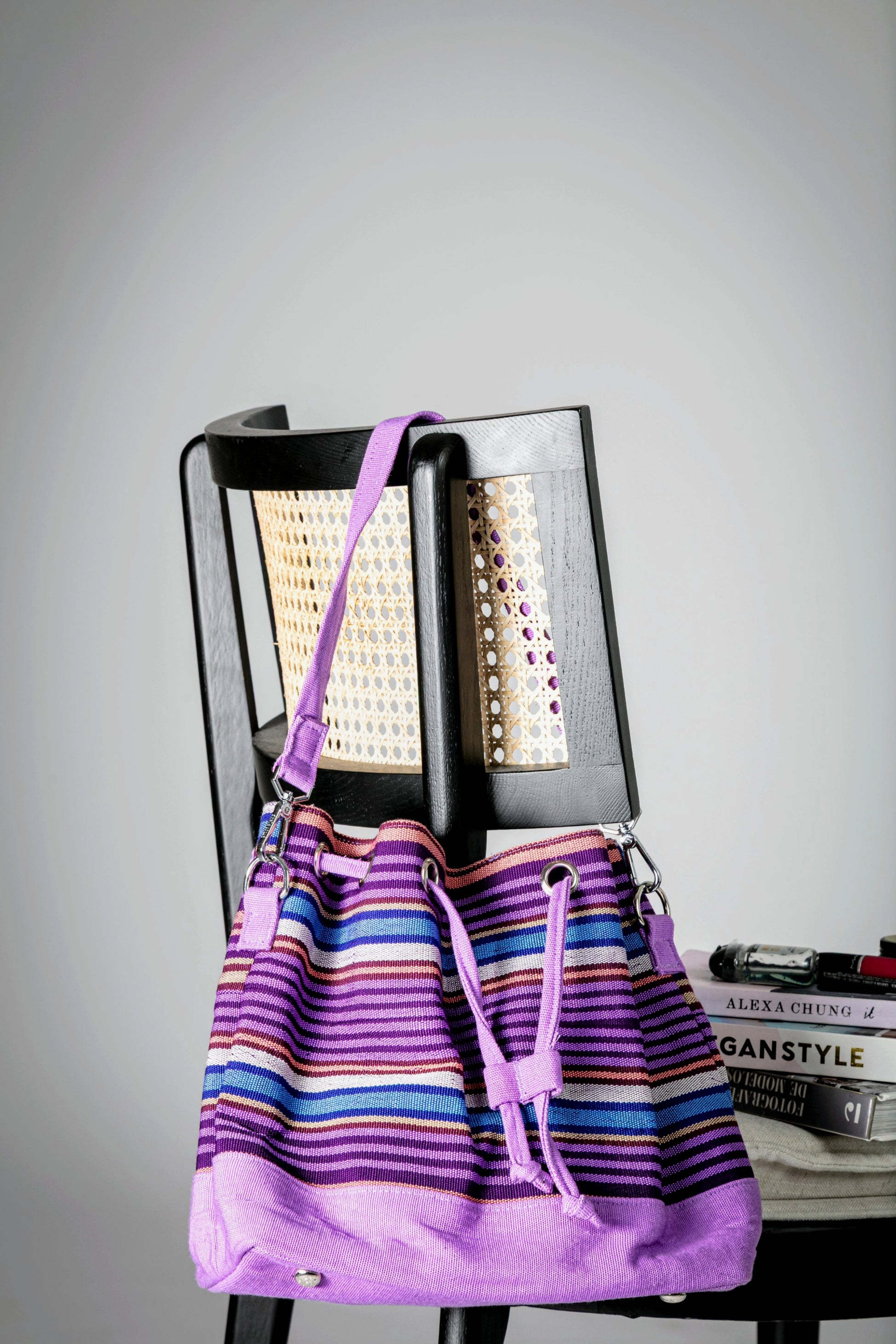 Purple and multicolor striped bucket bag with a short strap and drawstring closure hanging on a chair
