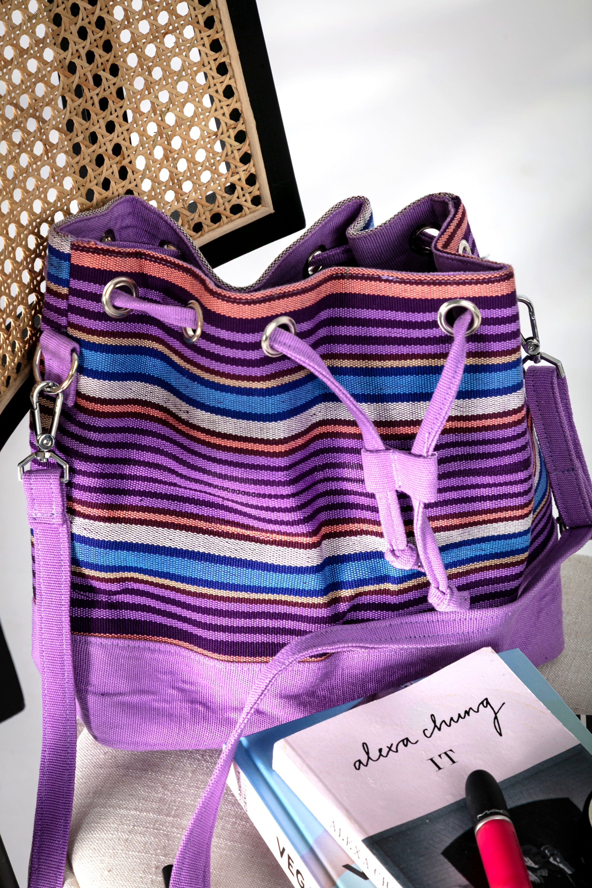 Purple and multicolor striped bucket bag with a drawstring closure on a chair
