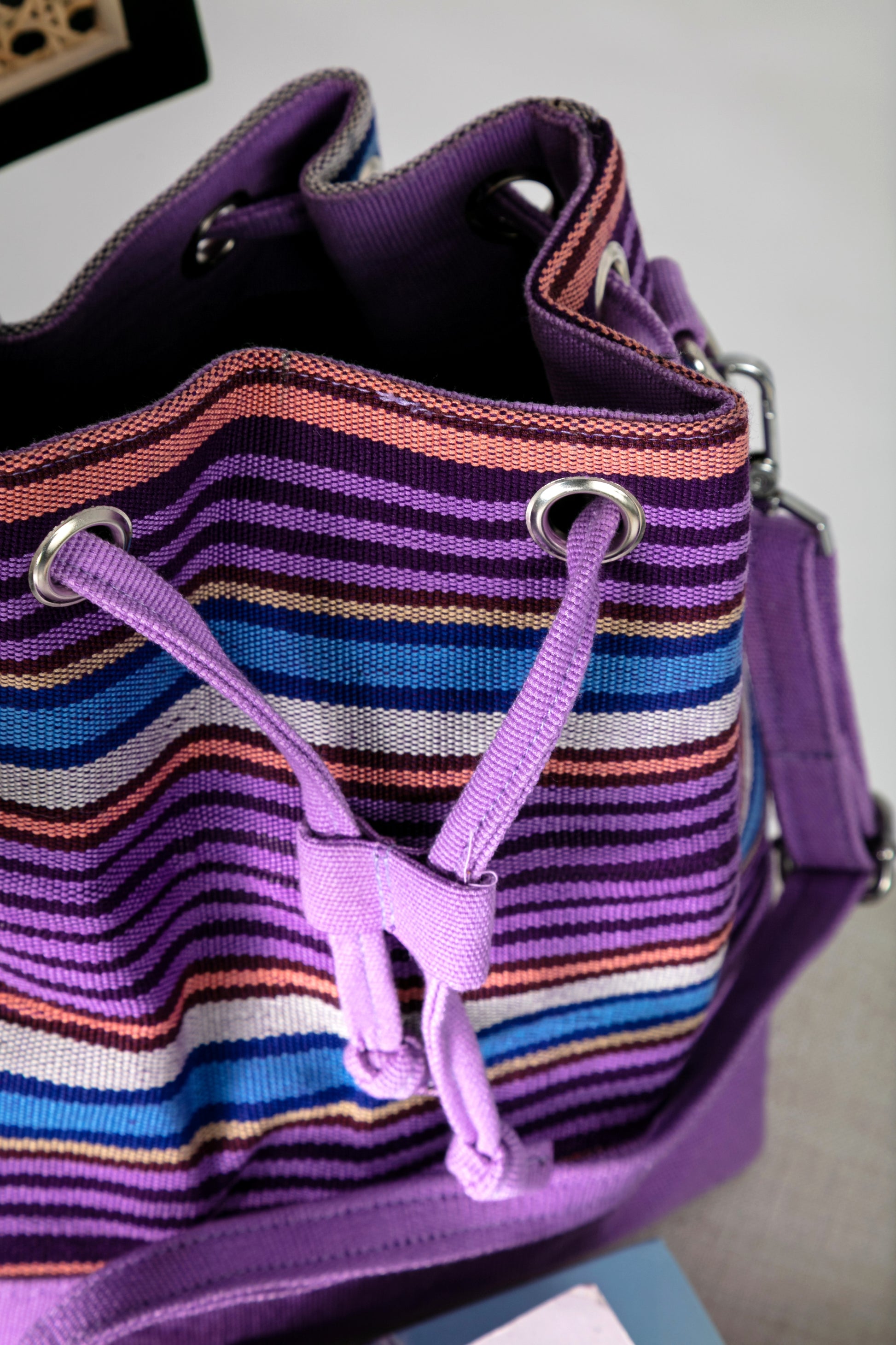 Top view of purple and multicolor striped bucket bag with a drawstring closure on a chair